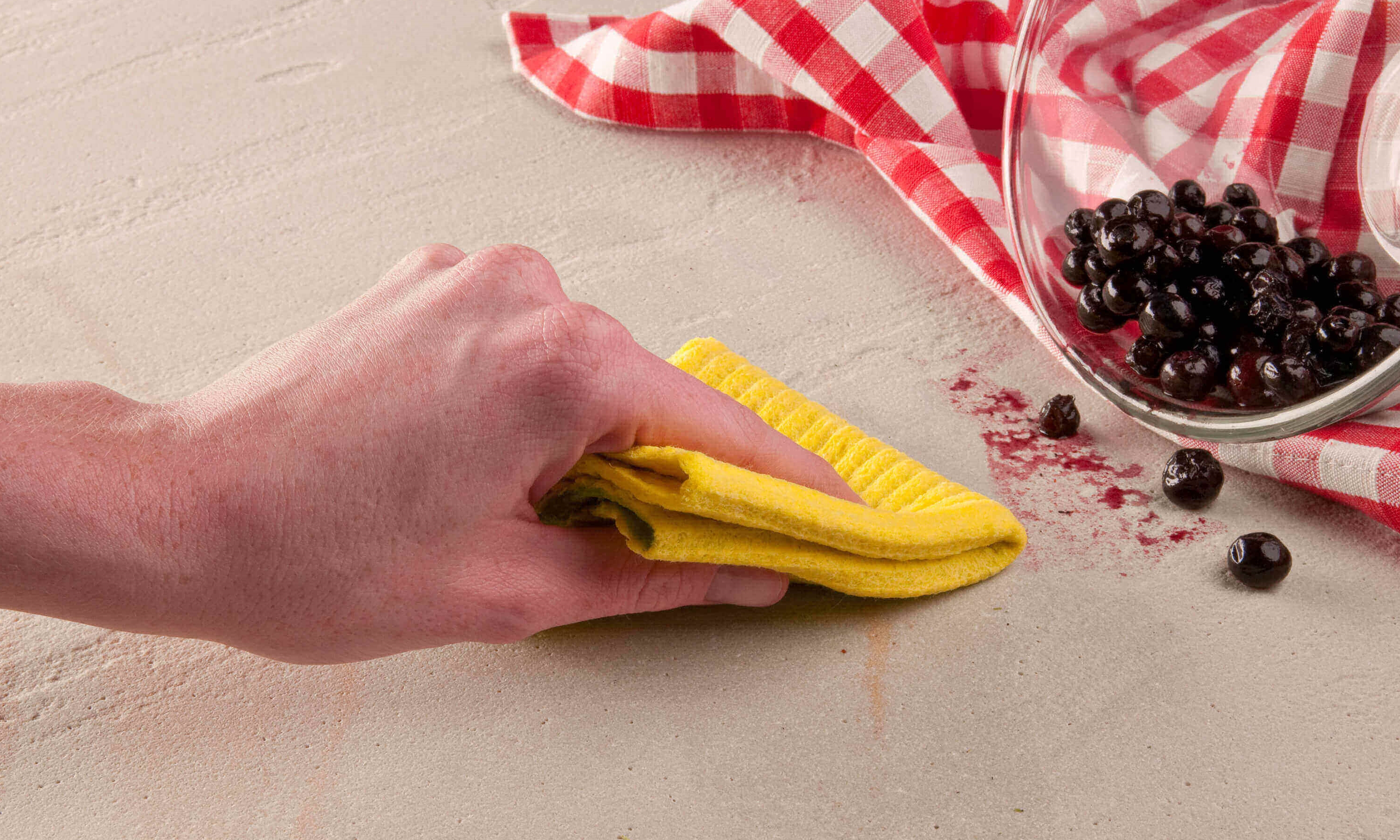 Hand wischt Beerenfleck mit gelbem Tuch weg
