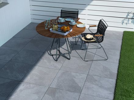 Terrasse mit Gartenmöbeln und hellen Platten in Schieferoptik im Halbschatten