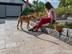 Frau sitzt auf Beetrand, vor ihr steht ein Hund, Terrassenbelag aus Travertinplatten in sanften Brauntönen