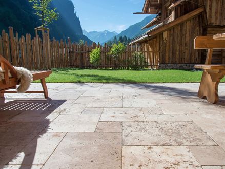 Terrassenboden mit Travertin Rustic und Holzmöbeln, im Hintergrund eine Rasenfläche und Ausblick auf die Berge