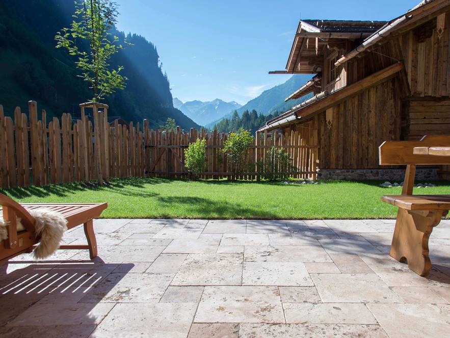 Terrassenboden mit Travertin Rustic und Holzmöbeln, im Hintergrund eine Rasenfläche und Ausblick auf die Berge