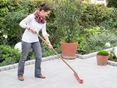 Eine Frau reinigt eine Granitterrasse mit dem Besen, im Hintergrund ein naturnaher Garten