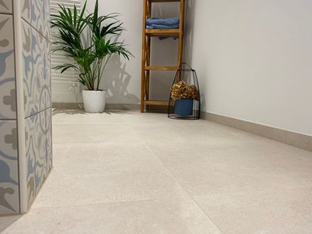 Modernes Bad mit Holzmöbeln, Dekopflanze und hellen Fliesen in Kalksteinoptik