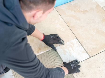 Mann verlegt Travertinfliesen in hellem Beige im Römischen Verband