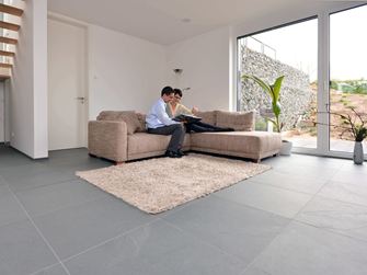 Grossformatige Schieferfliese Grey Slate im Wohnzimmer mit heller Couch und weissen Wänden. Ein Paar sitzt auf der Couch