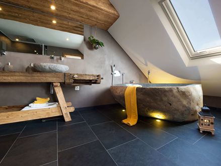Rustikales Bad mit Badewanne in Steinoptik und dunklen Schieferfliesen als Bodenbelag