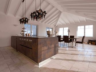 Kücheninsel mit Weinflaschenhalterung an der Decke, im Hintergrund Esstisch und Stühle auf verlegtem Travertin Light mit getrommelter, ungespachtelter Oberfläche