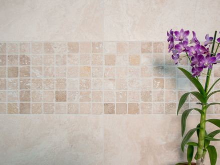Orchidee vor Mosaik-Wand mit hellem Travertin