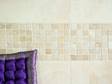 Travertin Mosaik von Travertin Fliesen umrahmt, davor ein lila Kissen