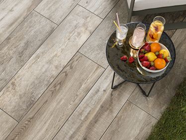 Terrasse avec table d'appoint, sur laquelle sont posés fruits et boissons, et dalles en grès cérame aspect bois vues du dessus