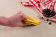 Eine Hand wischt Naturstein mit einem gelben Tuch ab, in der Ecke eine ausgeleerte Schale mit Beeren