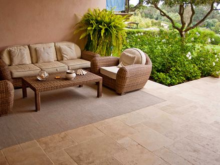 Eingangsbereich eines mediterranen Hotels mit Korbsesseln, Travertin als Bodenbelag und einem grünen Garten im Hintergrund