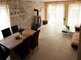 Ess- und Wohnzimmer mit hellen Natursteinfliesen, einer Wand mit Natursteinverblender und Holzmöbeln