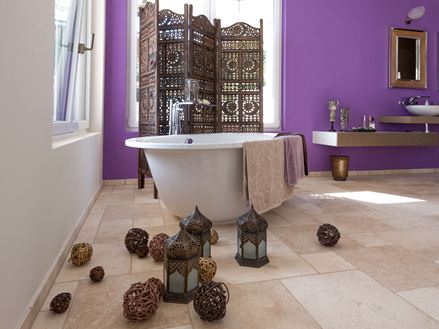Fliesen aus Travertin Light in einem Bad mit freistehender Badewanne und lila Wand im Hintergrund