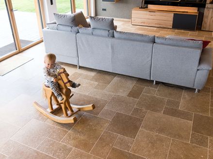 Kind sitzt auf Schaukelpferd und spielt im Wohnzimmer mit Travertinboden Noce SELECT