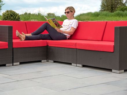 Frau sitzt auf modernen Couchmöbeln mit roten Sitzkissen auf einer Blausteinterrasse