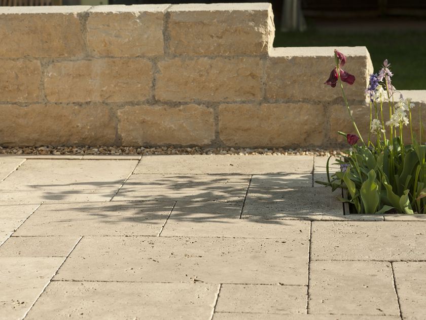 Travertinplatte Medium Select mit Natursteinmauer und Blumen im Hintergrund