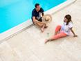 Paar sitzt am Pool auf Travertinterrasse