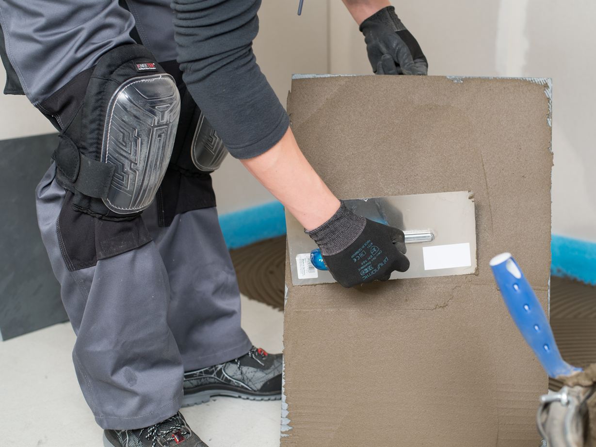 Ein Fliesenleger bestreicht eine Fliesen von der Rückseite mit Kleber