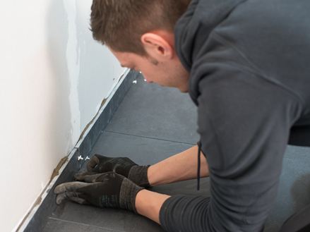 Fliesenleger bringt Sockelleisten an