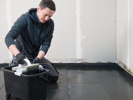 Fliesenleger kniet auf dem verlegten Schieferboden und wäscht den überschüssigen Fugenmörtel ab
