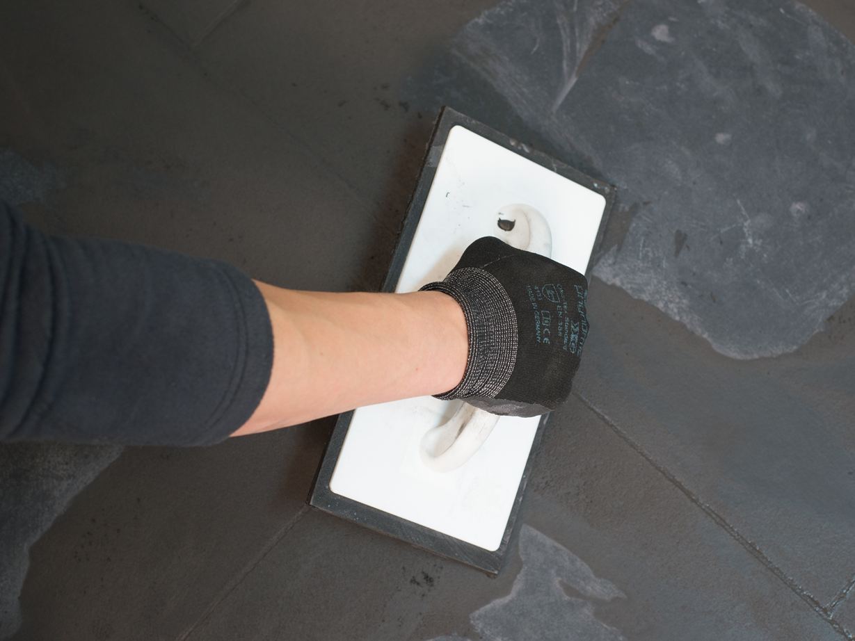 Fugen von dunklen Fliesen werden verspachtelt