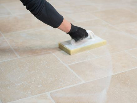 Fugenmörtel wird mit einem Schwammbrett von verlegten Travertinfliesen abgewaschen