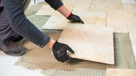 Ein Fliesenleger verlegt eine Travertinfliese