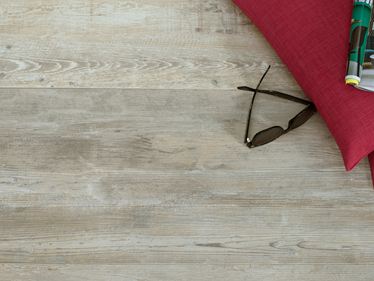 Helle Platten aus Feinsteinzeug in Holzoptik mit Brille und rotem Kissen