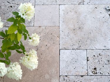Beige Travertinplatten im Römischen Verband verlegt mit weißen Blumen von oben