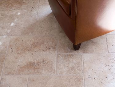 Travertinfliese Medium im römischen Verband, getrommelt, darauf ein brauner Sessel